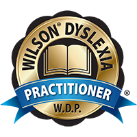 Gold badge with an open book at the center, surrounded by the words "Wilson Dyslexia Practitioner" and the initials "W.D.P." A blue ribbon with the word "Practitioner" runs across the badge.