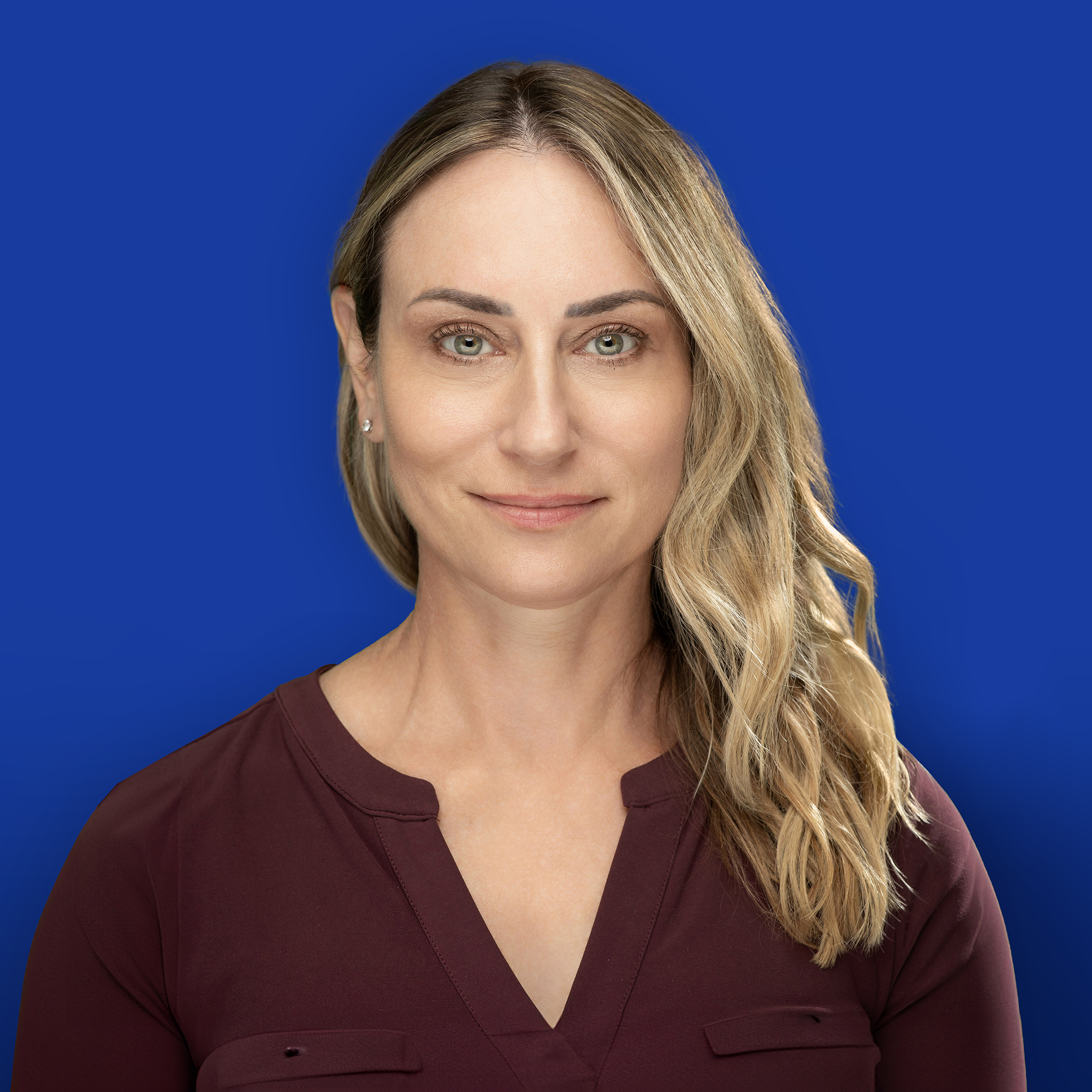 Professional headshot of a blonde woman in a maroon shirt.