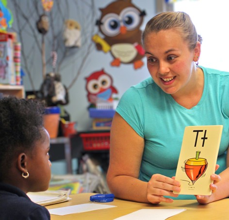 Teacher showing a student a flash card with a spinning top on it and the letter T
