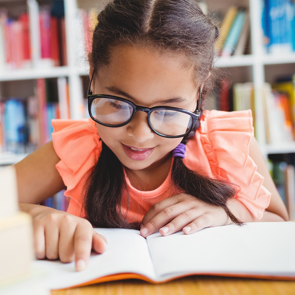 smiling student wearing glasses and pointing to text on the page of the book she is reading